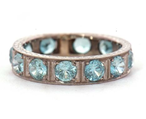 A zircon eternity ring. the 5mm wide band set throughout with round blue zircons, all set in unmarked white metal (tests as a