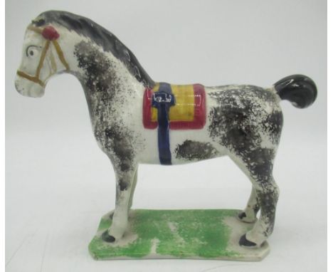 Prattware model of a horse, sponge decorated with black, blue ocre and red saddle and tack. on shaped rectangular green spong