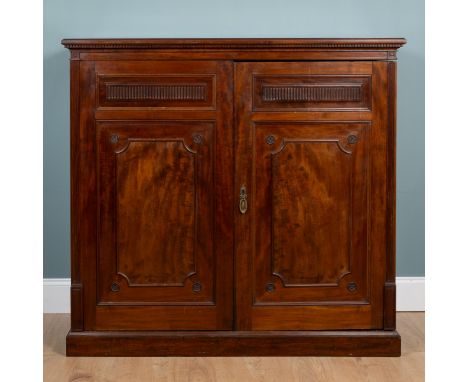 A 19th century mahogany low linen press The dentil cornice above two panelled doors opening to reveal four sliding shelves, a