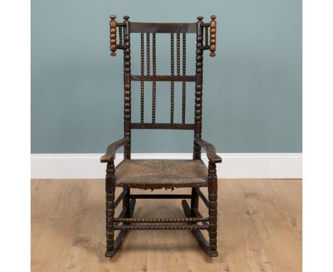 In the manner of Ernest Gimson An ash-framed, bobbin-turned rocking chair with a wing back and wicker seat. 55cm wide x 111cm