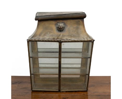 A brass wall-mounted display cabinet The sarcophagus-form top with a lion mask mount above a three-shelf interior with a mirr