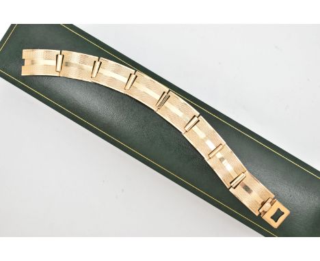 A YELLOW METAL ARTICULATED BRACELET, designed as a series of eight rectangular, engine turned pattern links, with an integrat
