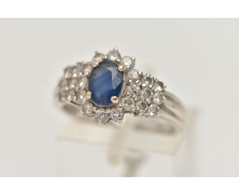 AN 18CT WHITE GOLD SAPPHIRE AND DIAMOND CLUSTER RING, centrally set with an oval cut blue sapphire, in a four claw setting, v