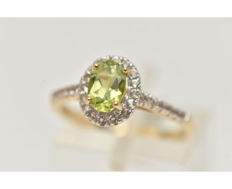 A 9CT GOLD PERIDOT DRESS RING, a principally set oval cut peridot, prong set in yellow gold, set with a surround of round cut