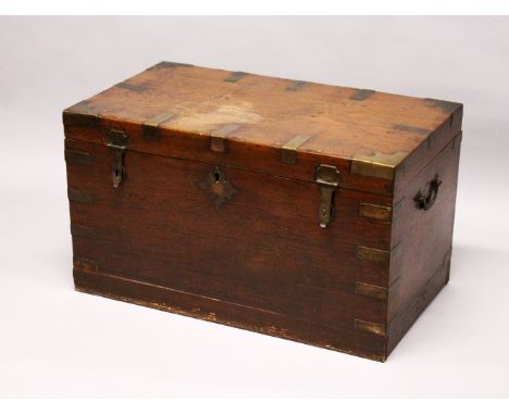 A GOOD 19TH CENTURY ANGLO INDIAN TEAK AND BRASS BOUND TRUNK, the rising top opening to reveal an interior fitted with carved 