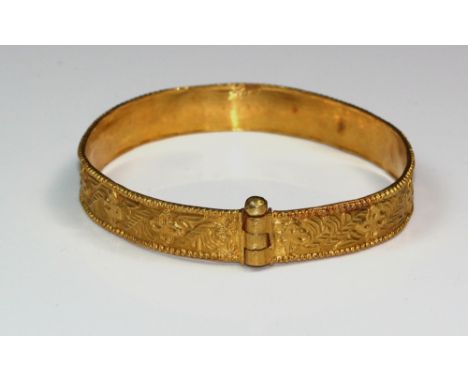 An Indian or Middle Eastern yellow metal broad bangle chased with stylised flowers and leaves between beaded borders, unmarke