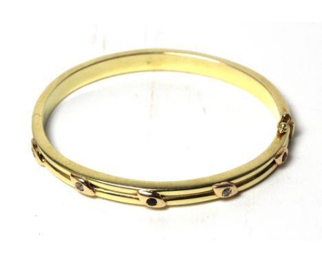 A Continental yellow metal and gem set hinged bangle of hollow twin tubular construction, the front designed as five leaf mot