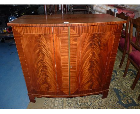 A cross-banded boxwood strung Mahogany bow fronted Cupboard, the flame Mahogany pair of opposing doors with brass beading rev
