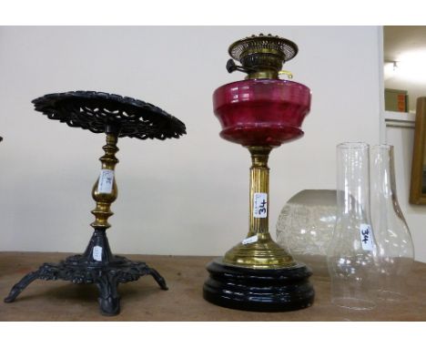A cranberry glass oil lamp with brass column together with a brass and painted metal trivet (2)