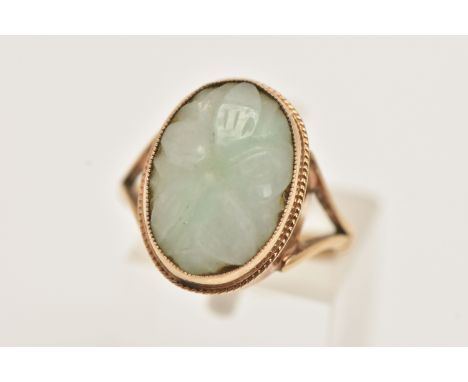 A 9CT GOLD JADE RING, the oval jade panel carved to depict a flower, to the rope twist surround and bifurcated shoulders, 9ct