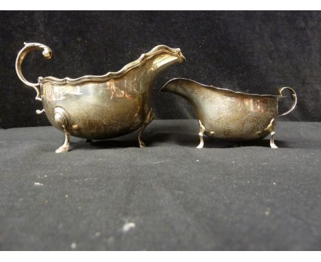 Two silver sauce boats, eached with barbed rim and on three hoof form feet, the larger with retailers mark of Boodle and Dunt