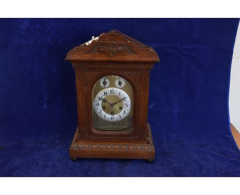 A Junghans oak cased mantel clock with carved pediment and bevelled glazed door opening to reveal a brass back plate with chi