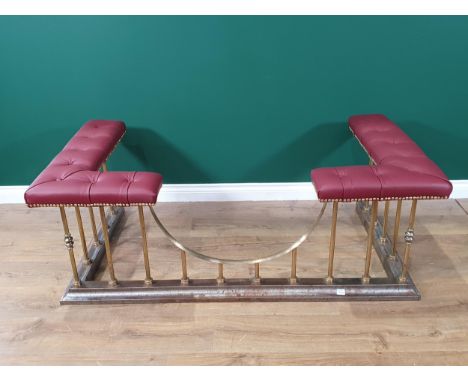 A red button upholstered brass and steel Club Fender, raised on spindles and shaped plinth support, 54in L x 1ft 8in H x 2ft 