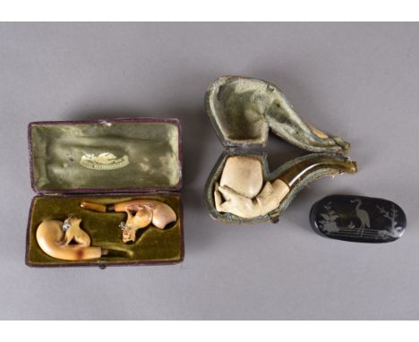 A 19th Century cased meerschaum pipe, carved as a hand holding an egg, amber stem, case (af), together with a pair of carved 