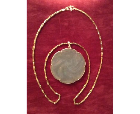 A PALE GREEN JADE ROUNDEL  In flowerhead form, mounted in 22ct yellow gold on a 22ct gold chain, the clasp marked '22k'. (d 5