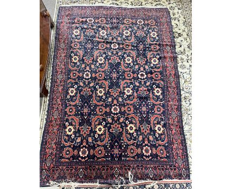A Persian Senneh wool floor rug with large central panel decorated with geometric and floral motifs on a dark blue background