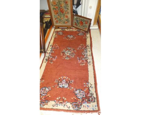 An oriental style rug in shades of terracotta and cream, 180 x 95cm, together with an oak framed fire screen with needlework 