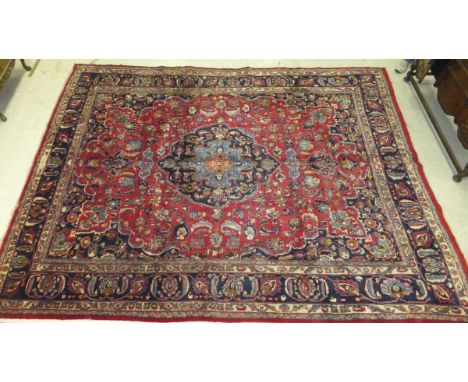 A Persian carpet, the central floral decorated medallion in dark blue, light blue, orange, cream and red, on a red floral dec