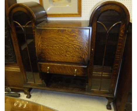 A 1920's oak secretaire cabinet, the central fall front bureau with single drawer over a shelf, flanked by two domed glazed c