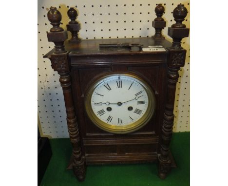 A circa 1900 oak cased mantel clock with pilaster and ball finial decoration, the white enamel dial bearing Arabic numerals