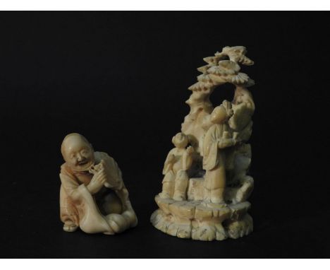 An ivory netsuke of a crouching woman holding a fan, and a carved figure group of three figures beneath a tree