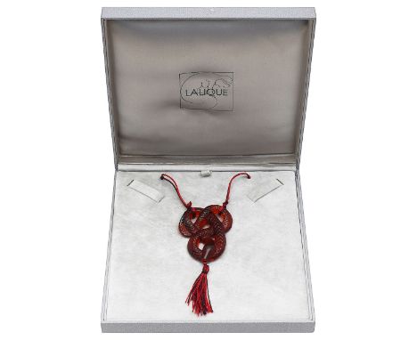 A red snake pendant by Laliquein the form of a coiled snake, with scale details, suspended from maroon and red cord, terminat