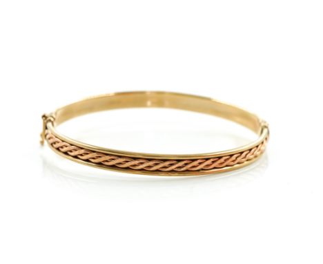A 9CT TWO COLOUR GOLD BANGLEWith interwoven Celtic inspired decoration within plain borders, on a sliding clasp, on a foldove