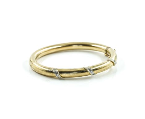 A  GOLD AND DIAMOND SET BANGLEOf oval hinged form, the front mounted with three rows of three circular cut diamonds in a slan