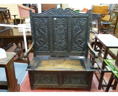 A HIGHBACK CARVED OAK BOX SEAT BENCH, the triple panel back with shaped top rail and mythical creatures flanking a ribbon and