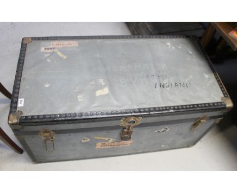 A vintage silver metal travel trunk with black and silver metal banding, with the remnants of various travel labels to includ