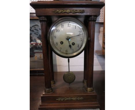 An oak cased circular mantel clock supported within an open pergola of four Doric columns and tableau with brass trim, the si