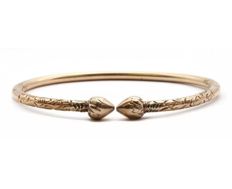 A gold torque bangle, round wire bangle, 3.60mm, with hand engraved decoration and tapered finials, tested as approximately 9