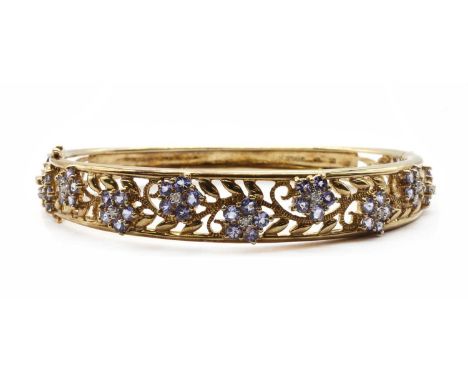 A 9ct gold tanzanite and diamond bangle, the pierced upper half claw set with graduated clusters of brilliant cut diamonds an