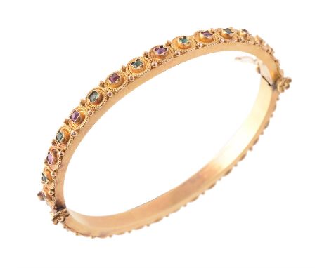 A mid 19th century ruby, emerald and gold Etruscan Revival bangle, circa 1875, the hinged bangle alternately set all around w
