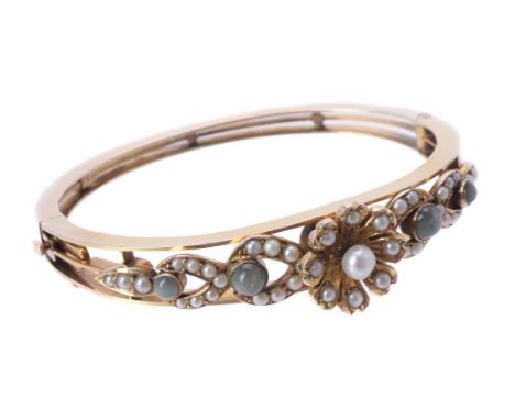 An Edwardian half pearl and cat's eye chrysoberyl hinged bangle, circa 1910, the central half pearl flower head above a taper