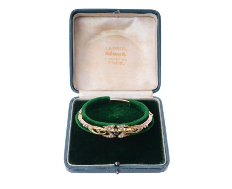 An Edwardian 15 carat gold, sapphire and half pearl bangle, circa 1905, the Art Nouveau scroll top set with half pearls aroun