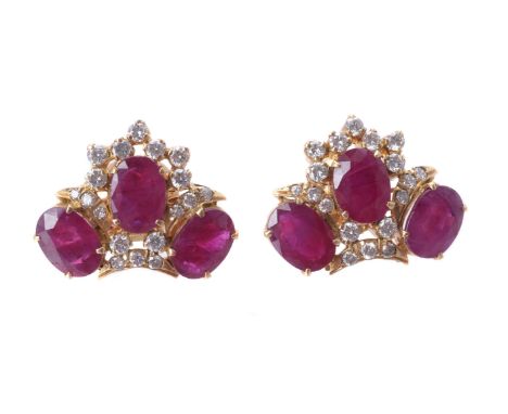 A pair of ruby and diamond ear studs, claw set with three oval mixed cut rubies within brilliant cut diamond borders, approxi