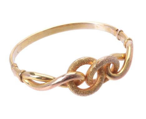 A gold coloured knot hinged bangle, the front section with two intersecting floral decorated hoops, to polished twisted shoul