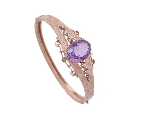 An amethyst and half pearl hinged bangle, the oval cut amethyst claw set above a pierced gallery, to pierced shoulders each s