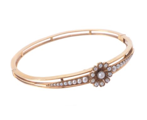 A late Victorian gold and half pearl hinged bangle, circa 1900, the central half pearl flower head to tapered half pearl set 