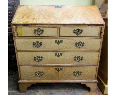 A Georgian oak and elm veneered bureau of three long and two short graduated drawers, the fall flap enclosing a fitted interi