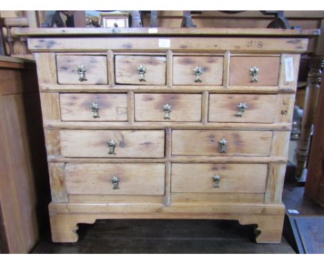 A small antique stripped pine chest fitted with an arrangement of eleven drawers flanked by panelled sides raised on bracket 