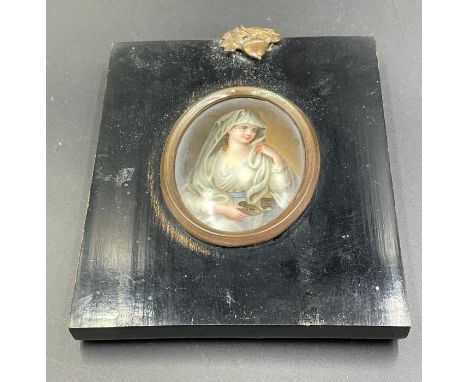 A framed small portrait on porcelain of a lay holding an oil lamp.