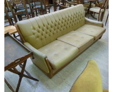 A 1960s teak finished, showwood framed settee, having a level back and low, enclosed arms, button upholstered in cafe-au-lait