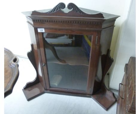 An Edwardian mahogany hanging corner cupboard, having a swan neck pediment, canted flanks with adjacent trinket shelves, the 