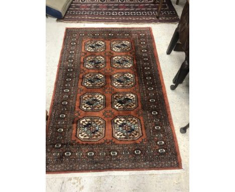 A modern Frith Rugs Bokhara rug, the central panel set with two rows of repeating elephant foot medallions on a terracotta gr
