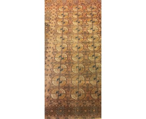 A Bokhara rug with three rows of elephant foot medallions on a rust red ground within a stepped red and black stylised tarant