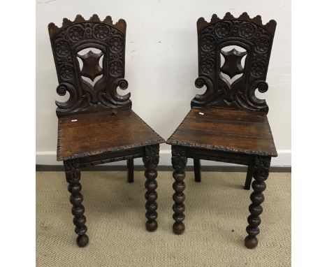 A pair of late Victorian carved oak panel seated hall chairs with flower head medallion and shield carved backs raised on bob