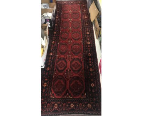 A Bokhara style runner, the central panel set with two rows of repeating medallions on a dark red ground within a stepped dar