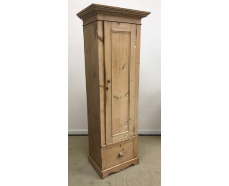 A slim pine cupboard with single panel door enclosing three shelves over a single drawer with turned knob handle raised on br